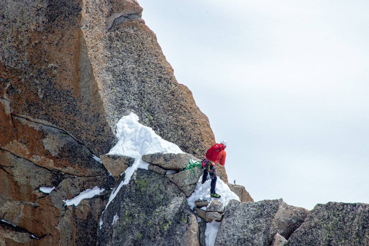 Climber adjusting basic mountain climbing gear including helmet on rocky ridge